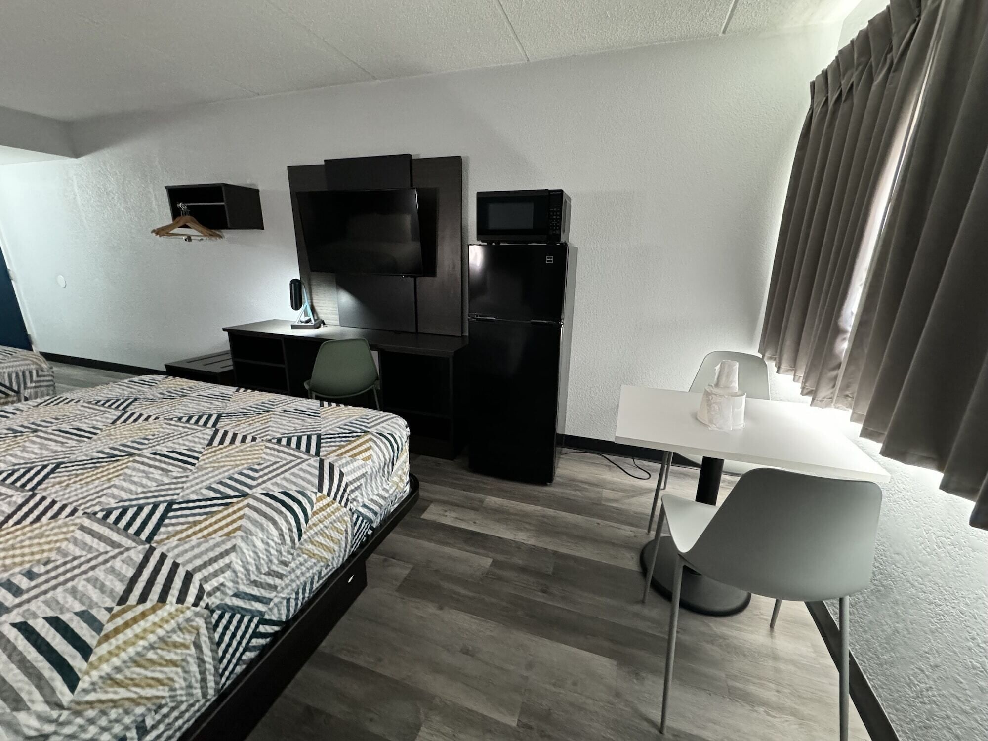 Habitación de hotel con cama, escritorio, silla, televisión y refrigerador.