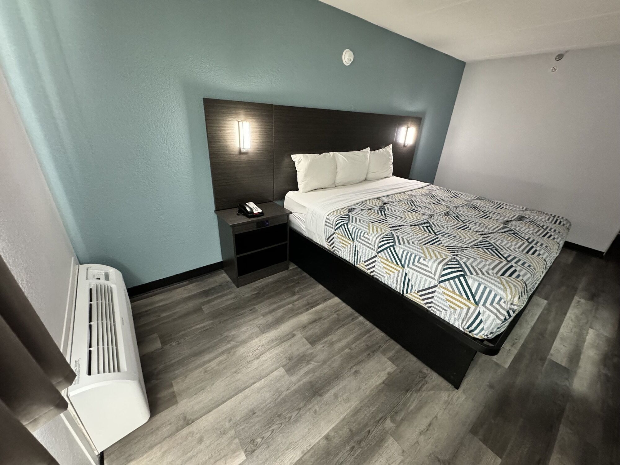 A hotel room with a bed, bedside table, and a wall-mounted heater.