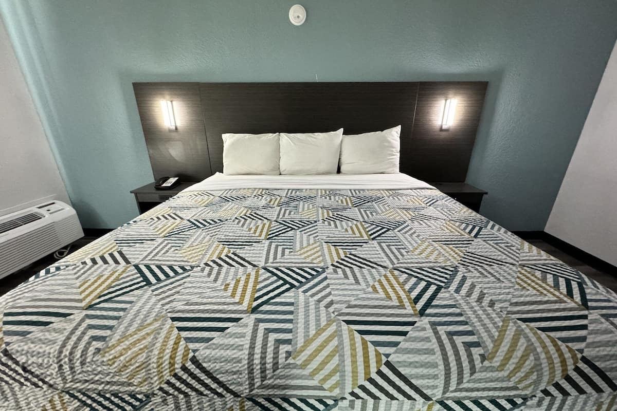 Una habitación de hotel con una cama grande, un cabecero oscuro, dos mesitas de noche y un aire acondicionado de pared.