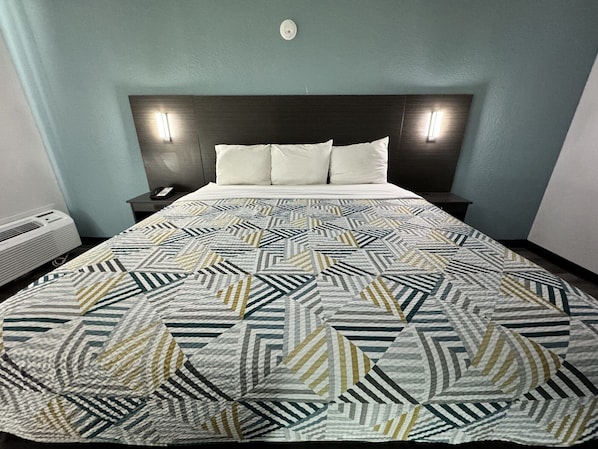 Una habitación de hotel con una cama grande, un cabecero oscuro, dos mesitas de noche y un aire acondicionado de pared.