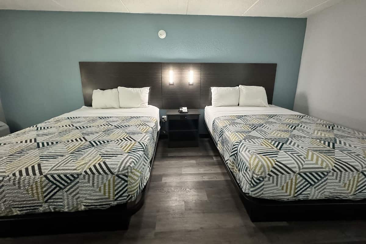 Habitación de hotel con dos camas, cada una con ropa de cama estampada, una mesita de noche, una lámpara de pared y una lámpara del techo.