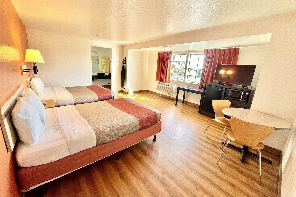 A hotel room with two beds, a desk, a chair, a TV, and a window with curtains.