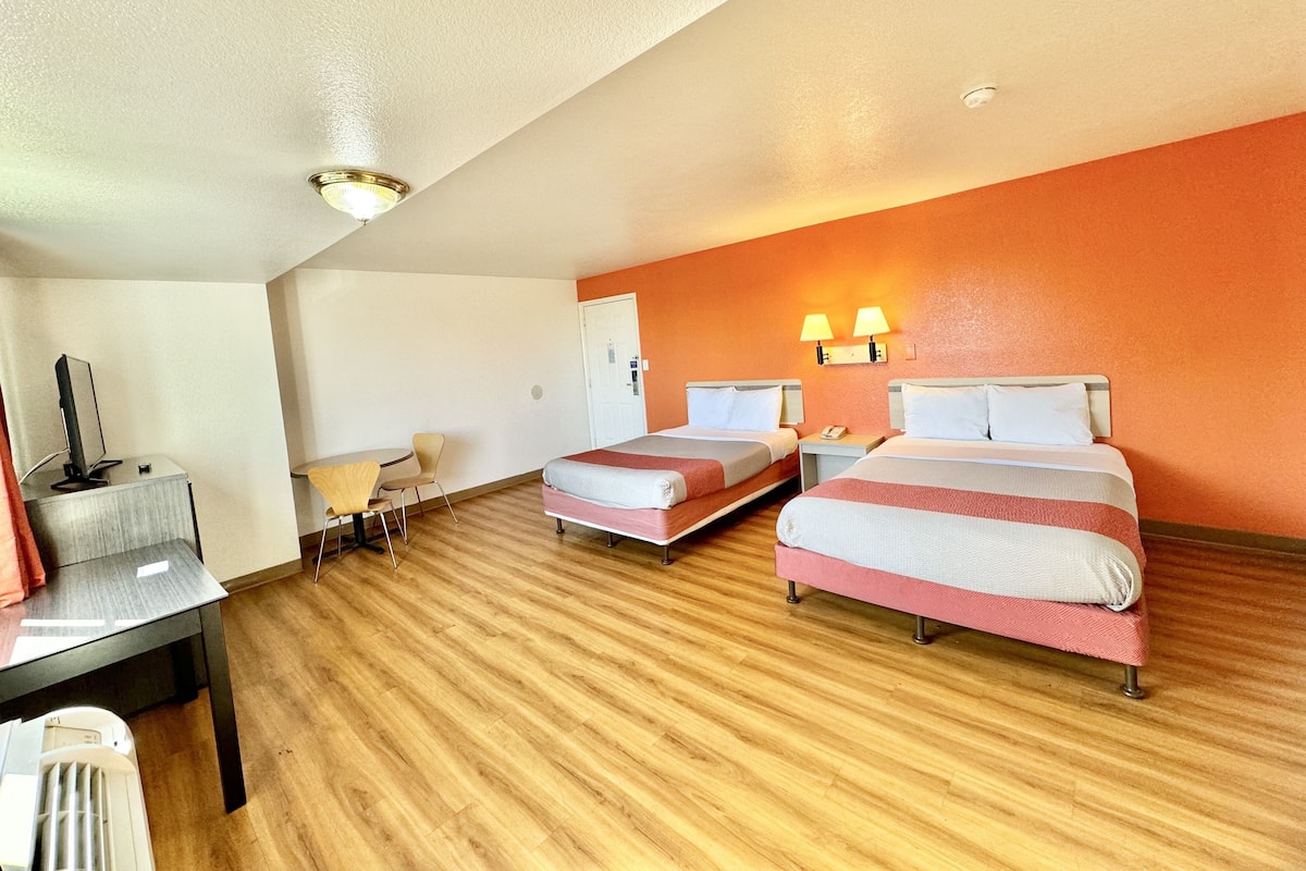 A hotel room with two beds, a desk, a chair, and a heater.
