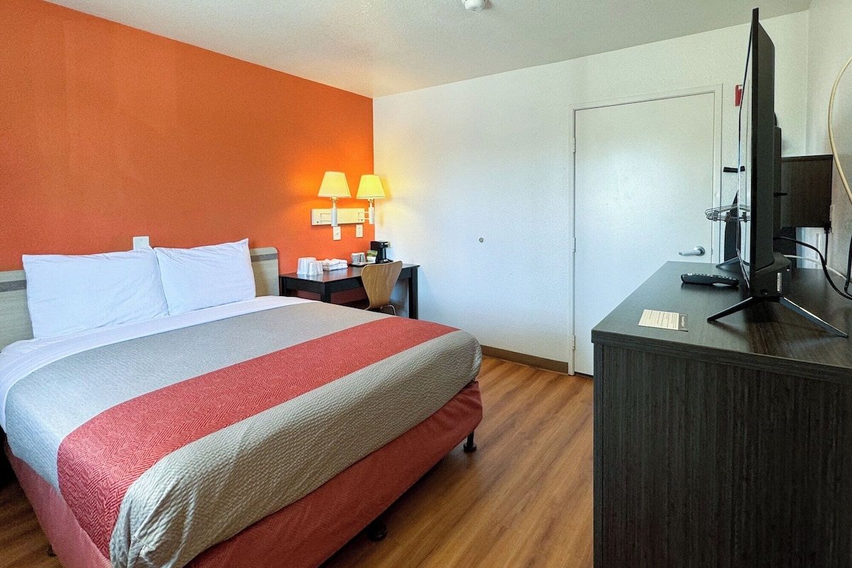 A hotel room with a bed, a desk with a computer, a TV, and a lamp.