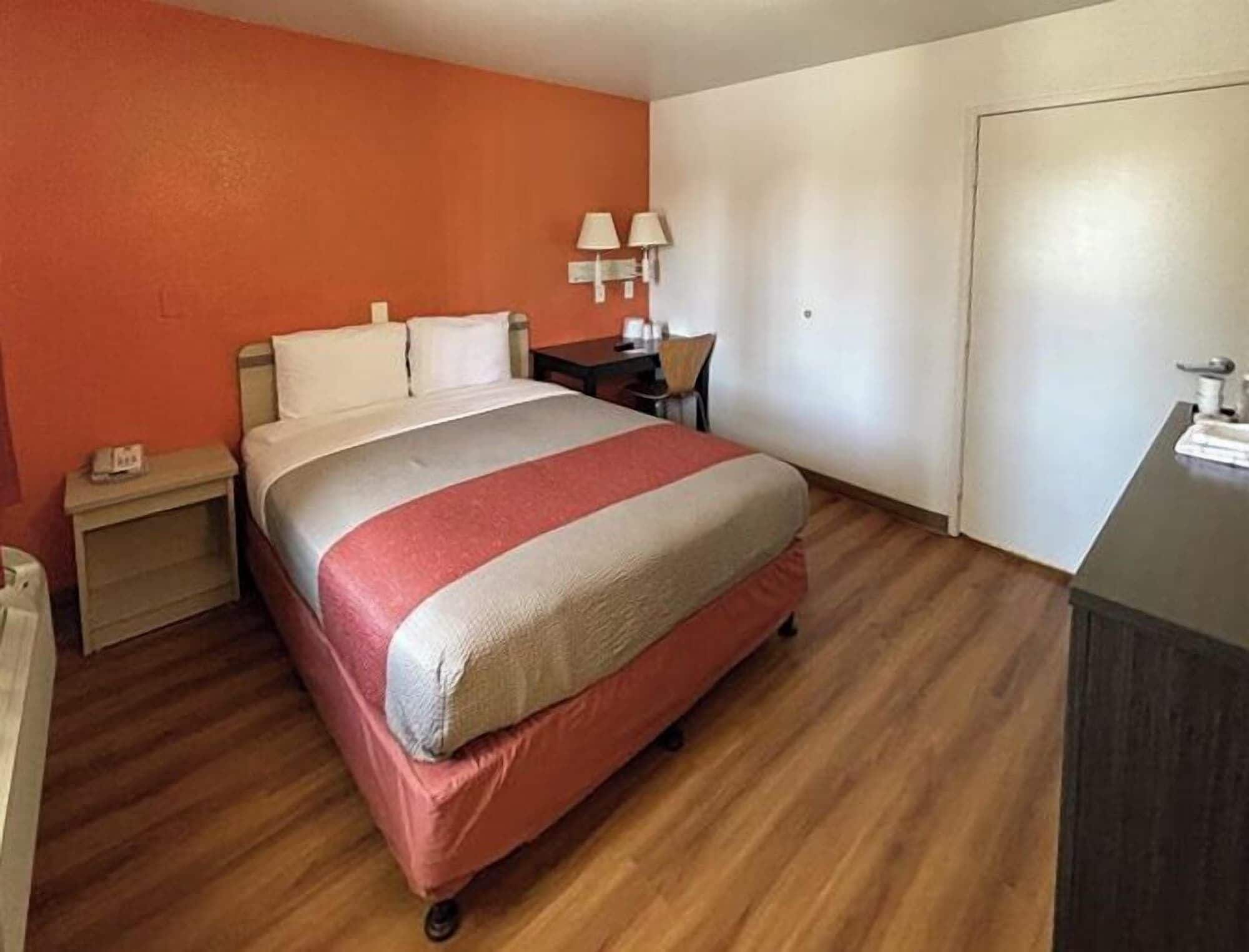 A hotel room with a bed, a nightstand, a desk, and a chair.