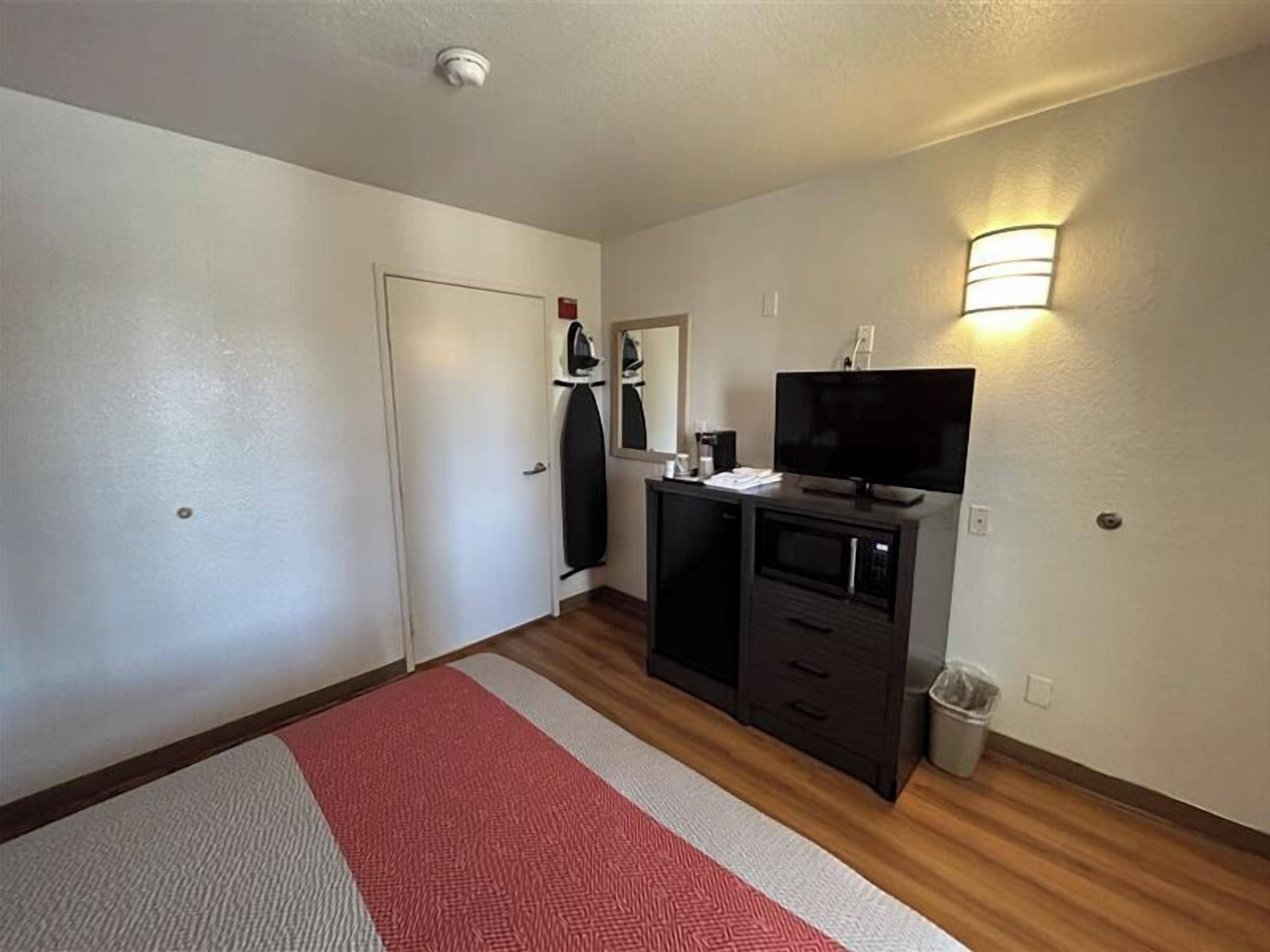 Una habitación de hotel compacta con kitchenette, televisor, microondas y un pequeño cubo de basura.