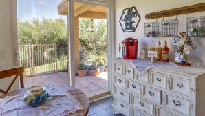 A room with a sliding glass door leading to a balcony with potted plants. There is a white dresser with multiple drawers and a coffee-themed wall decoration. - Palm Desert Vacation Rental w/ Community Pool! (Palm Desert)