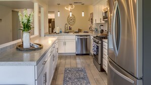 A modern kitchen with a central island, stainless steel appliances, and a decorative clock on the wall. - Palm Desert Vacation Rental w/ Community Pool! (Palm Desert)