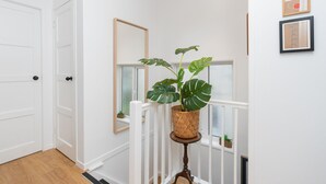 Passadís amb parets blanques, sòl de fusta, barana blanca i una planta en un petit moble.