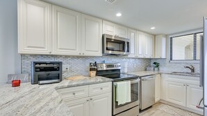 A kitchen with white cabinets, a granite countertop, stainless steel appliances, and a tiled backsplash.