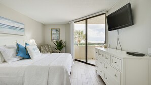 A bedroom with a bed, a TV, a dresser, and a balcony with a view.