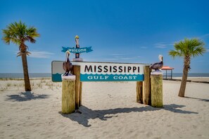 A wooden sign with 'Mississippi Gulf Coast' and a 'Welcome' sign on top, flanked by two wooden posts with bird sculptures, set against a beach backdrop. - Beachfront Gulfport Vacation Rental w/ Balcony! (Gulfport)