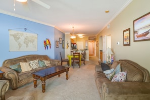 A living room with two sofas, a coffee table, a dining table with chairs, a world map on the wall, and a painting. - Beachfront Gulfport Vacation Rental w/ Balcony! (Gulfport)