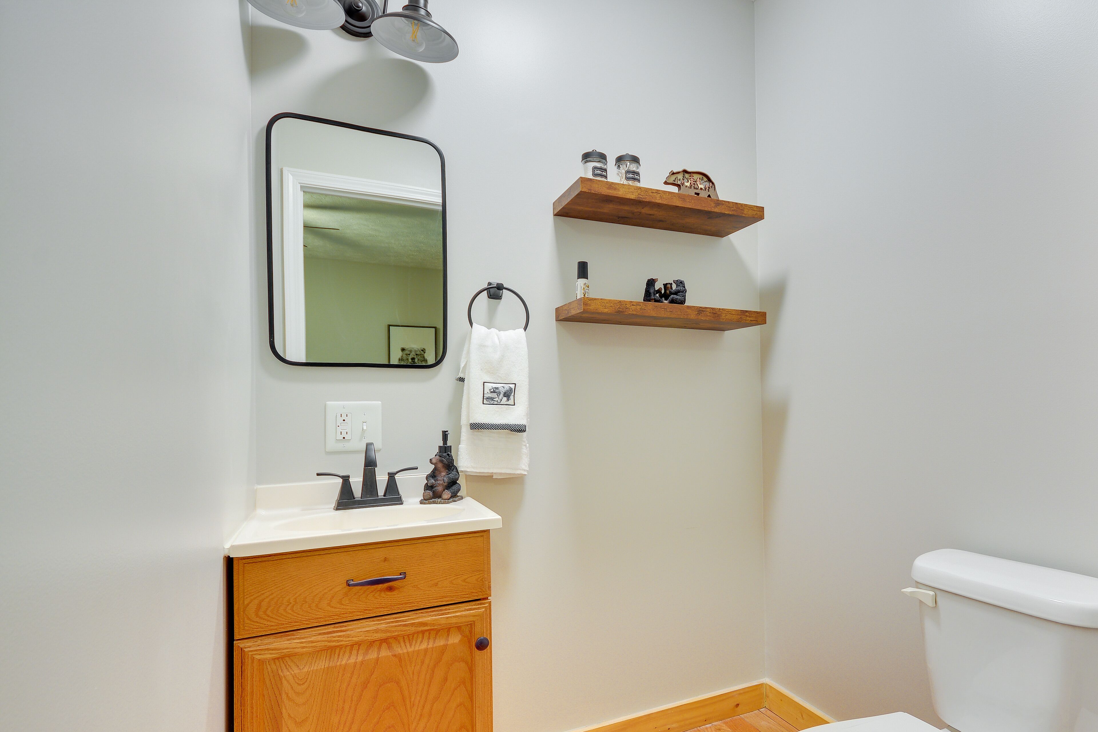 A bathroom with a wooden cabinet, a mirror, a toilet, and two wooden shelves with toiletries.