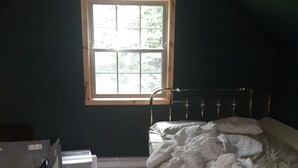Una habitación con una cama individual, una ventana, un radiador y una pequeña mesa.