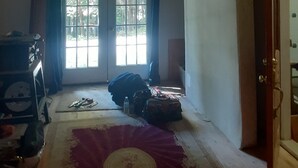 Una habitación con vigas de madera en el techo, un ventilador de techo, una ventana con cortinas y una cama con colcha estampada en rojo y blanco.