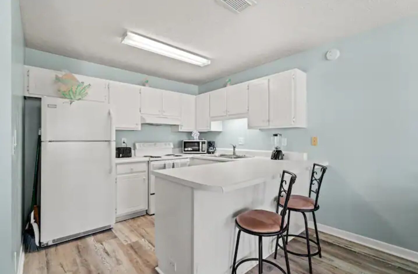 Una cocina moderna con armarios blancos, una isla central con taburetes y un microondas.