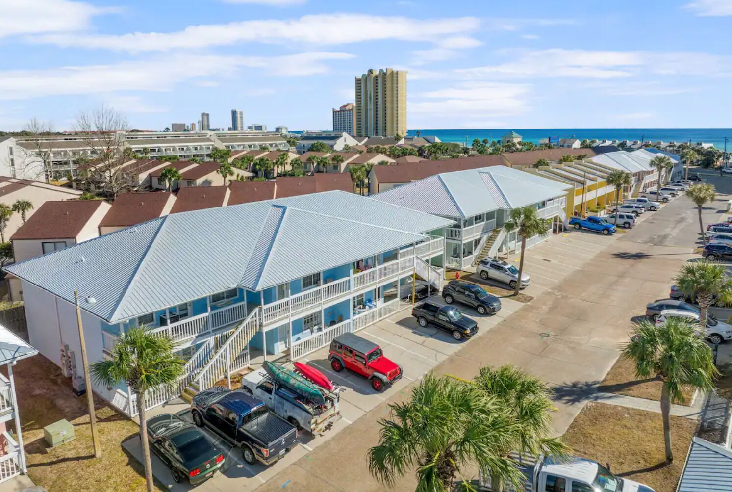 A hotel with a parking lot, multiple vehicles, and a view of the ocean.