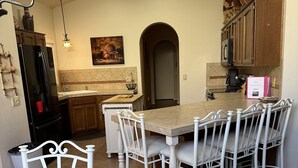 Una cocina moderna con comedor, que incluye una isla central, sillas blancas y un refrigerador negro.