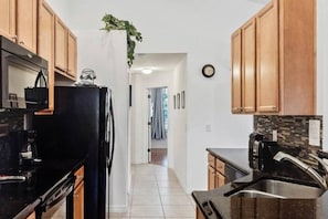A kitchen with wooden cabinets, a refrigerator, a coffee maker, and a sink. - Beautiful one story w/ pool home. Near Disney! (Kissimmee)