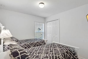 Ein Schlafzimmer mit zwei Betten, einem Fenster mit Jalousien, einer Tür und einer Deckenleuchte.