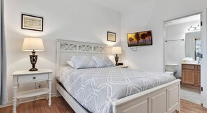 A neatly arranged bedroom with a bed, two bedside tables with lamps, a wall-mounted painting, and a door leading to a bathroom.