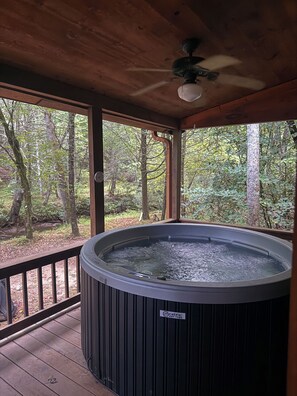 A hot tub in a wooden deck area with a view of a forest.