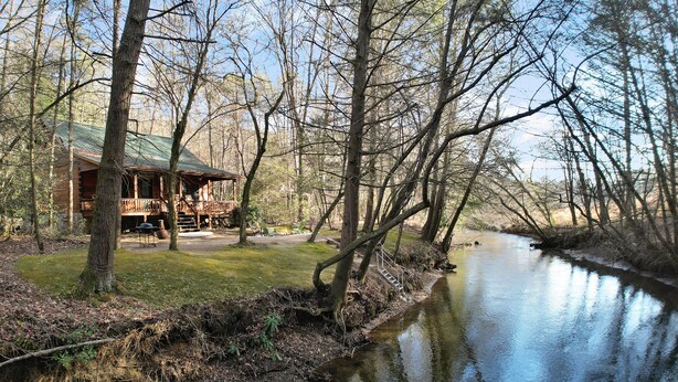Eine Hütte mit Veranda, einer kleinen Terrasse und einem Fluss.