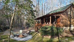 Eine rustikale Holzhütte mit Veranda, umgeben von Bäumen und einem Feuerstellenbereich mit Sitzgelegenheiten.