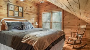 Ein Schlafzimmer einer Holzhütte mit einem Bett, einem Schaukelstuhl und einem Fenster mit Rollläden.