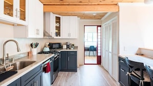 A modern kitchen with dark cabinets, a wooden ceiling, and a view to a dining area. - Guesthouse, Urban Oasis, 2b/2bth (Berkeley)
