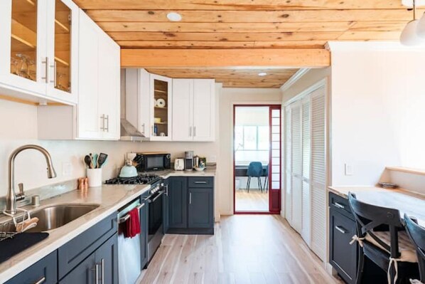 A modern kitchen with dark cabinets, a wooden ceiling, and a view to a dining area.