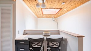 A compact kitchen with a wooden ceiling, a skylight, and a small dining area with two chairs. - Guesthouse, Urban Oasis, 2b/2bth (Berkeley)