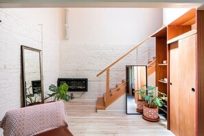 A spacious living area with a staircase, wooden flooring, and potted plants.