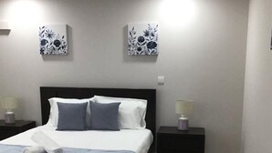 A neatly made bed with a white and blue bedspread, flanked by two black nightstands with lamps, in a room with grey walls and a tiled floor. - oceanview,  restaurants, beach , surrounded by mountains ,rivers and nature.  (Viana do Castelo)