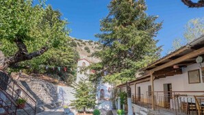 Un patio con una escalera de piedra, un edificio blanco de techo rojo y un árbol grande en el centro.