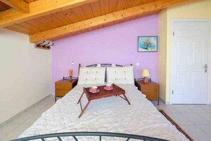 A bedroom with a bed, wooden headboard, bedside tables, a nightstand, a painting on the wall, and a door.