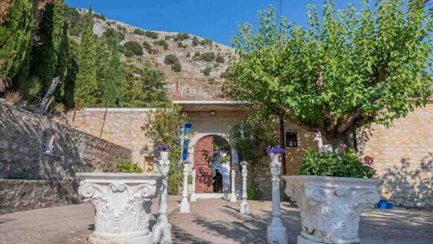 Una entrada con un arco de piedra, rodeada de columnas blancas y plantas en macetas.