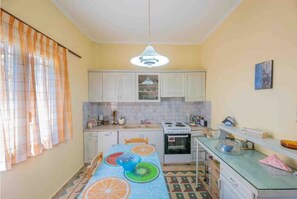 A compact kitchen with white cabinets, a stove, and a sink. There is a dining table with a colorful tablecloth.