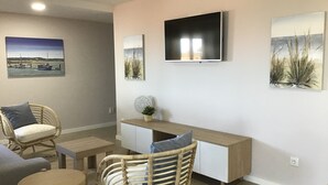 A modern living room with a flat-screen TV mounted on the wall, a sofa, a dining table, and two wicker chairs. - Pool with  oceanview, surrounded by nature, restaurants min to Viana do Castelo  (Viana do Castelo)