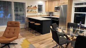 A modern kitchen with a central island, bar stools, a dining table with chairs, and a refrigerator. - Nordic Harbor | Haus Cabin (Center City)