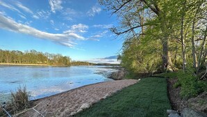 A grassy area with a sandy beach and a body of water, surrounded by trees. - Nordic Harbor | Haus Cabin (Center City)