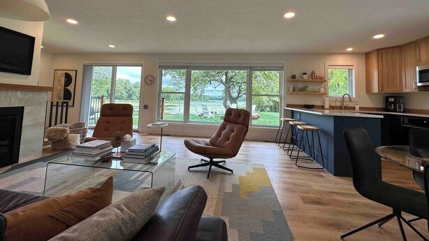 A spacious living room with a fireplace, a large window, and a kitchen area with wooden cabinets and a bar. - Nordic Harbor | Haus Cabin (Center City)