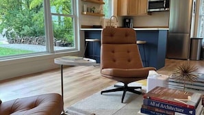 A modern kitchen with wooden cabinets, a stainless steel refrigerator, and a dining area with a brown leather chair and a glass coffee table. - Nordic Harbor | Haus Cabin (Center City)