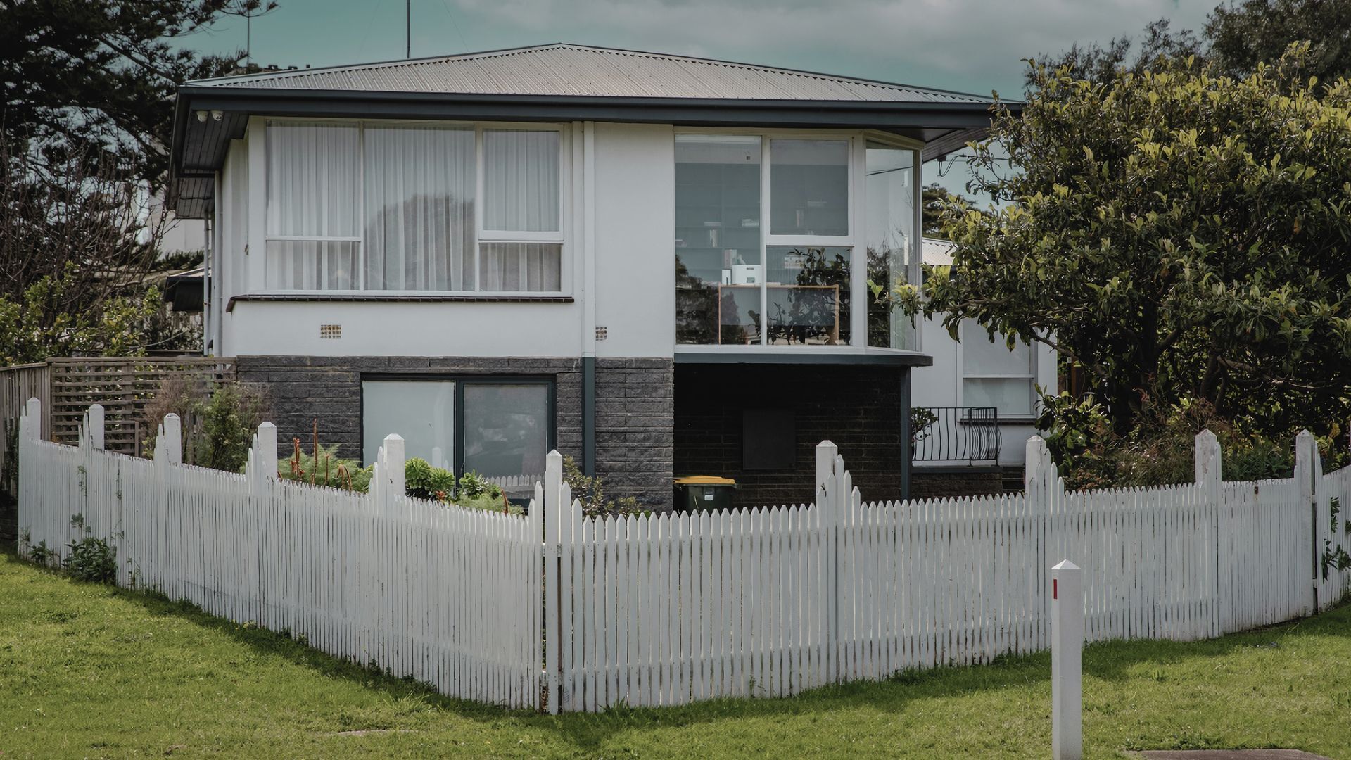 A two-story house with a white picket fence, a balcony, and a garage.