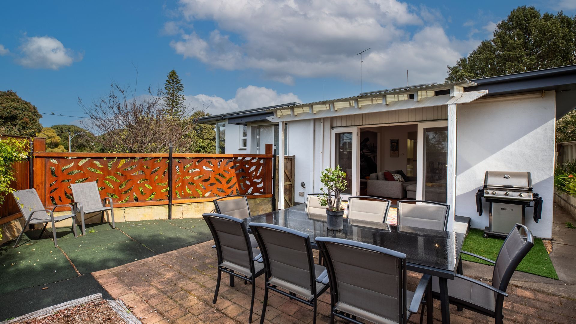 Een terras met een tafel, stoelen, een barbecue en een schuifdeur naar een woonruimte.