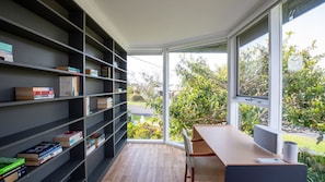 A modern reading nook with a large window, a bookshelf, and a desk.