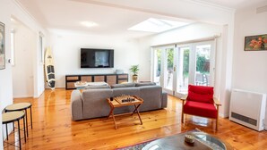 Ein Wohnzimmer mit einer Couch, einem roten Sessel, einem Schachbrett und einem Fernseher.