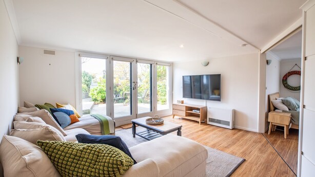 Ein modernes Wohnzimmer mit Sofa, Fernseher und Blick ins Freie.