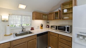 Una cucina moderna con mobili in legno, un lavello in acciaio inossidabile, una lavastoviglie, un forno a microonde e un frigorifero integrato.